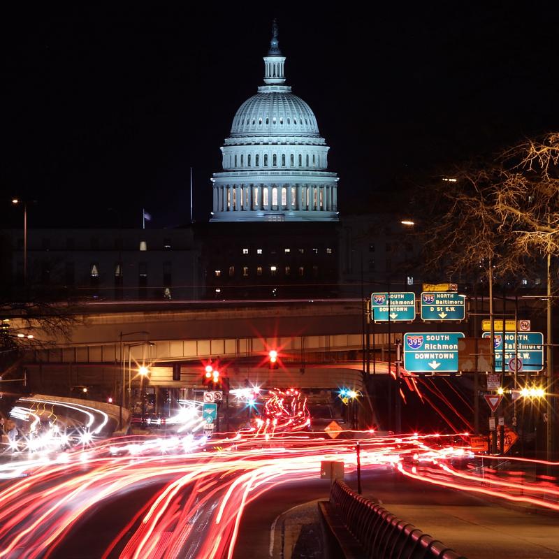 Nighttime view of the US Capitol building with a time-lapse of cars speeding by below