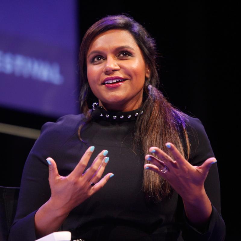Mindy Kaling speaking on stage in a black top