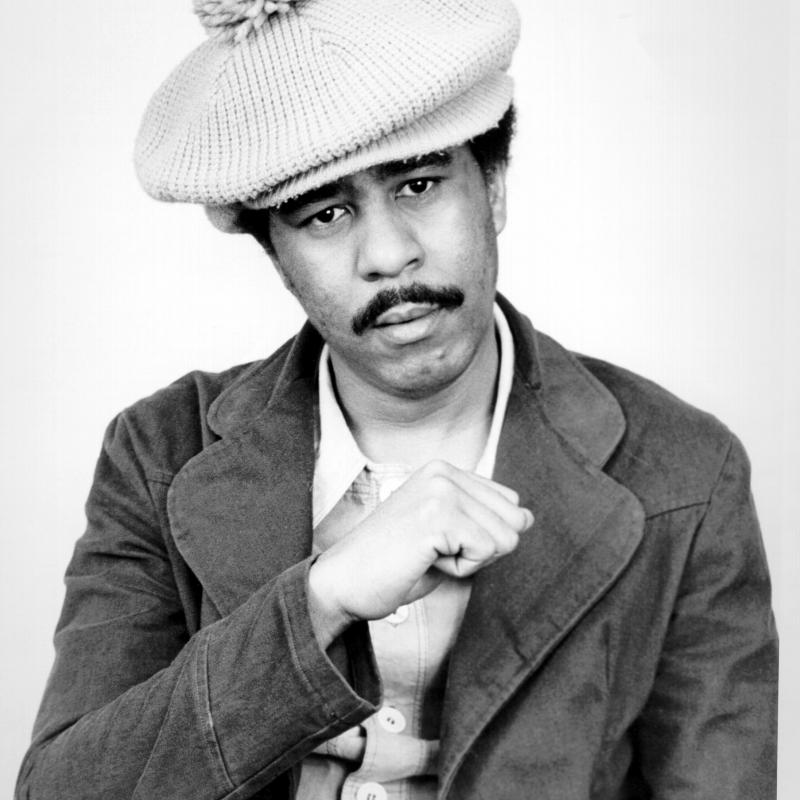 Comedian Richard Pryor making a fist and wearing a hat