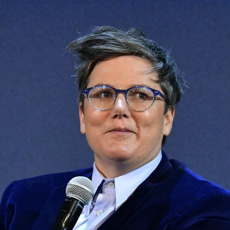 Comedian Hannah Gadsby smirks while holding a mic