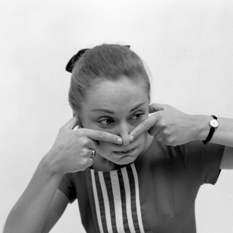 A woman pinches her nose and holds her breath in a black and white image