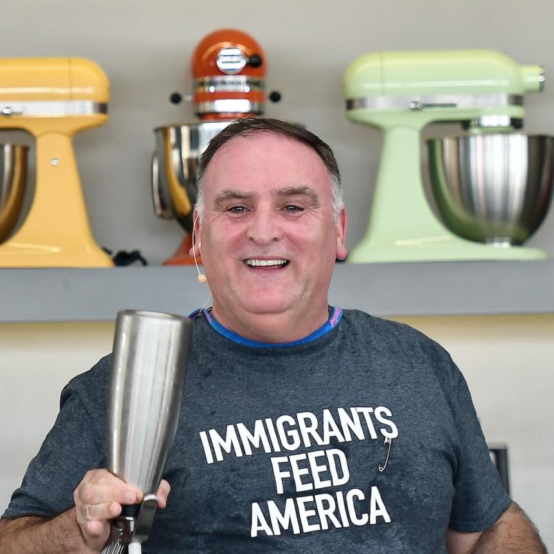 Chef Jose Andres stands at a table full of kitchen equipment wearing a shirt that says "Immigrants Feed America"