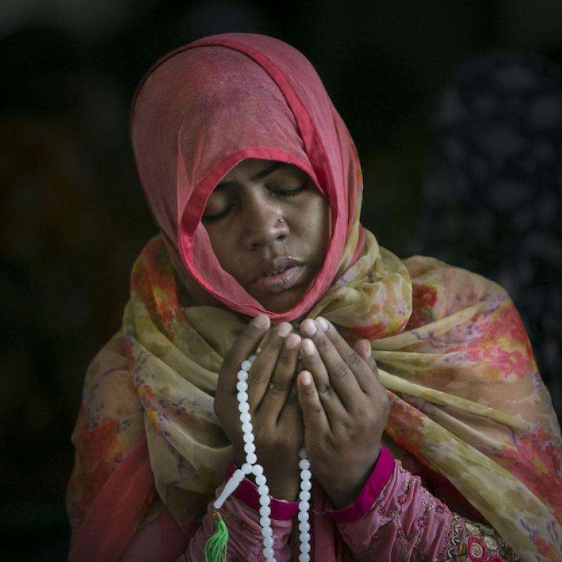 A Muslim girl praying with beads in a colorful headscarf