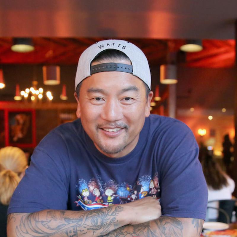 Chef Roy Choi smiles at the camera in a backwards hat with his arms crossed
