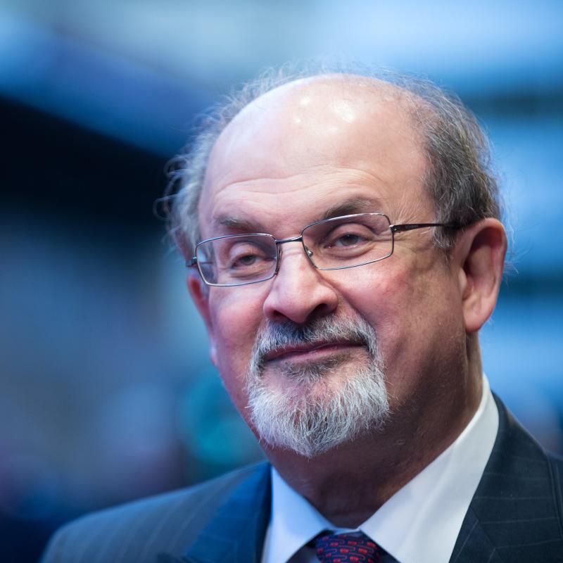 Author Salman Rushdie smiles slightly while wearing a suit