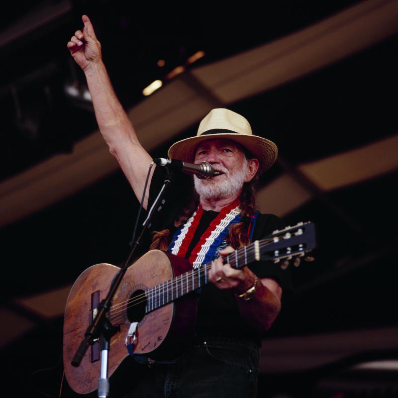 Musician Willie Nelson raises a finger to the sky as he plays his guitar on stage at a concert in 1994.