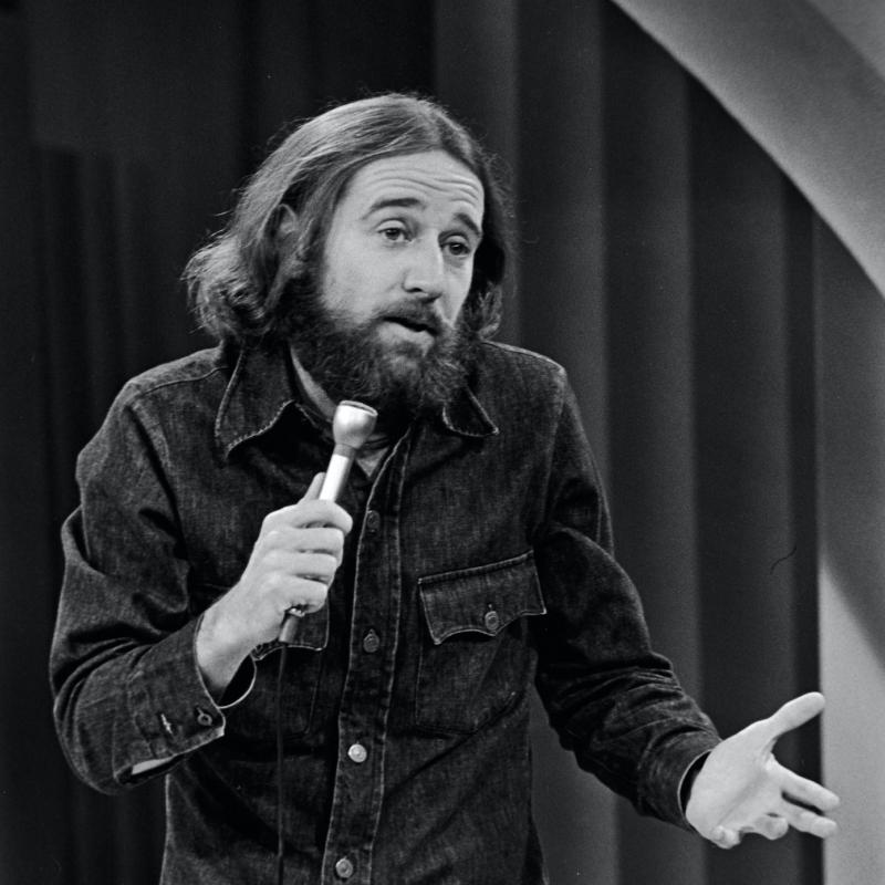 Comedian George Carlin tells a joke on stage in this image from 1981