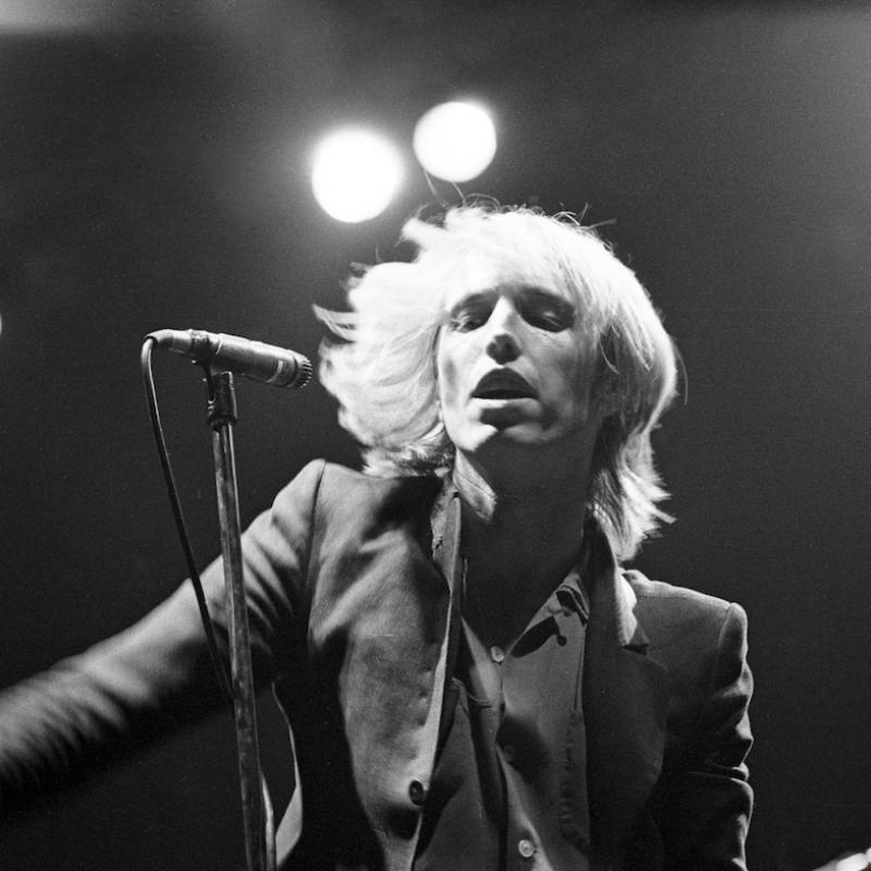 Famed musician Tom Petty tosses his hair on stage as he sings into a mic in this photo from his youth