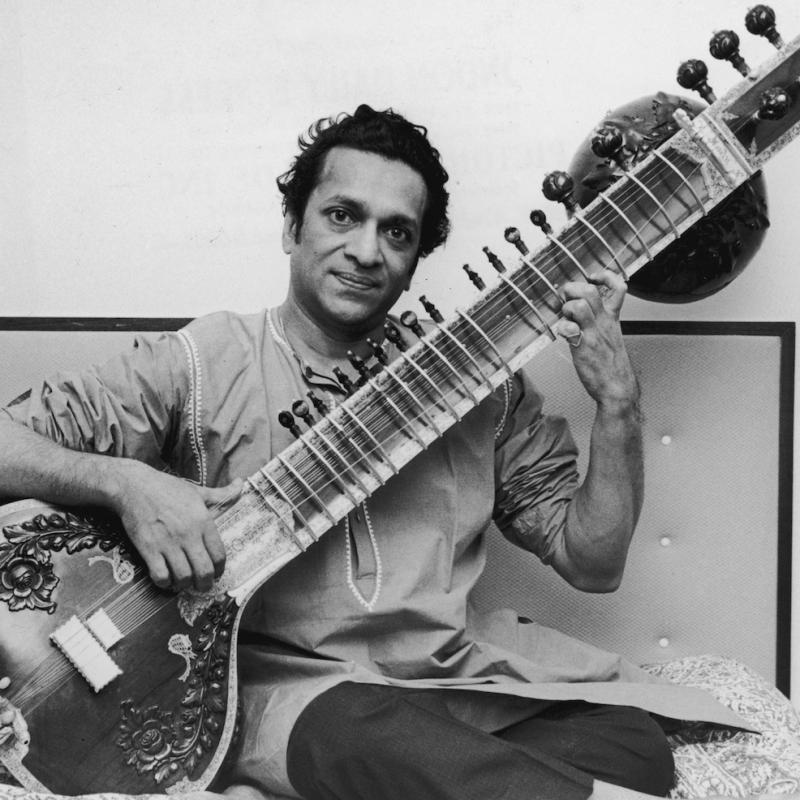 Famed sitar player Ravi Shankar sits on a bed with his sitar
