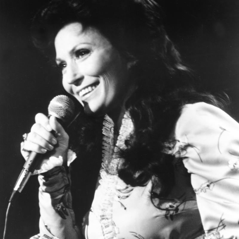 Black and white image of a young Loretta Lynn with a microphone
